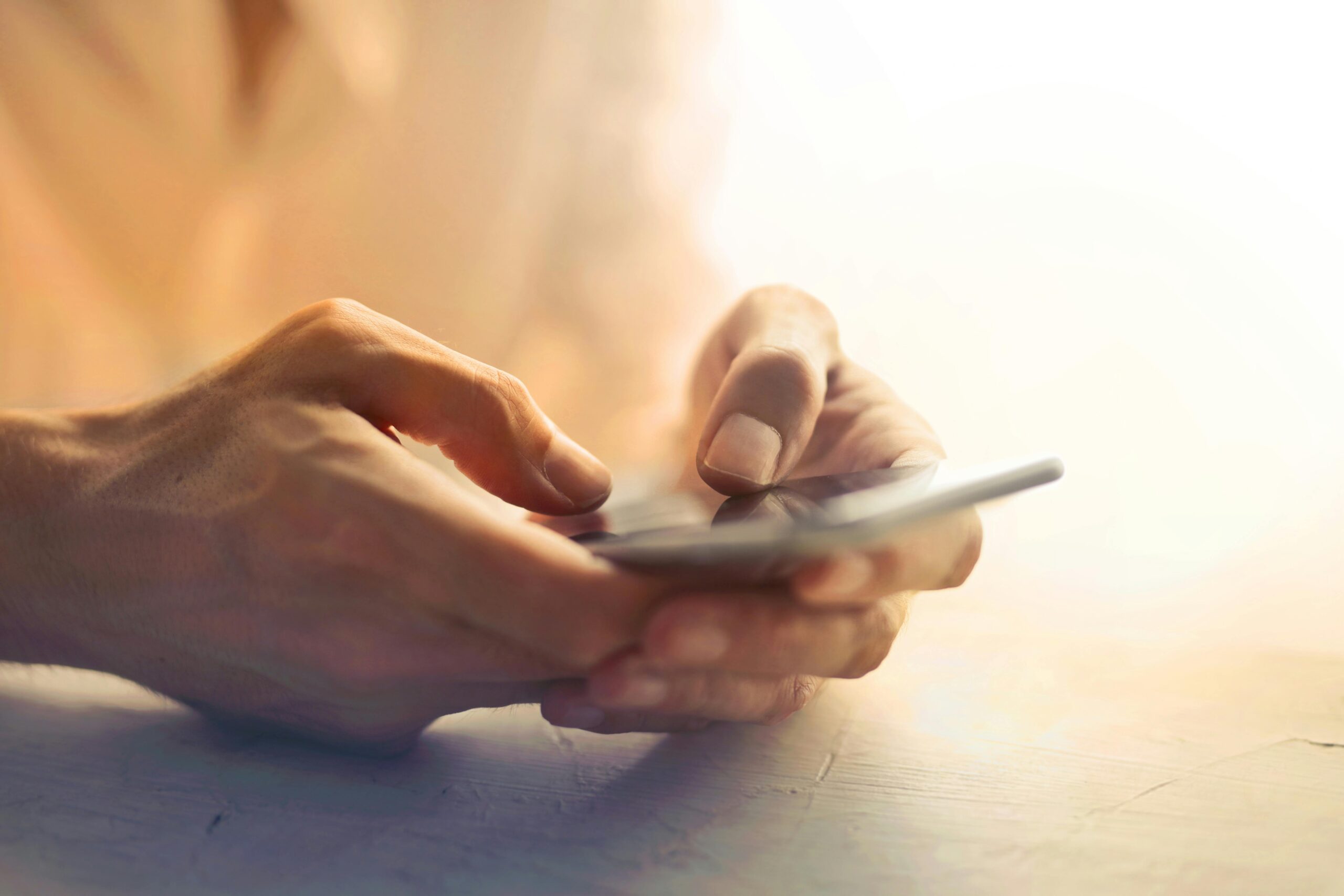 Detailed close-up of hands holding and using a smartphone indoors in soft lighting.