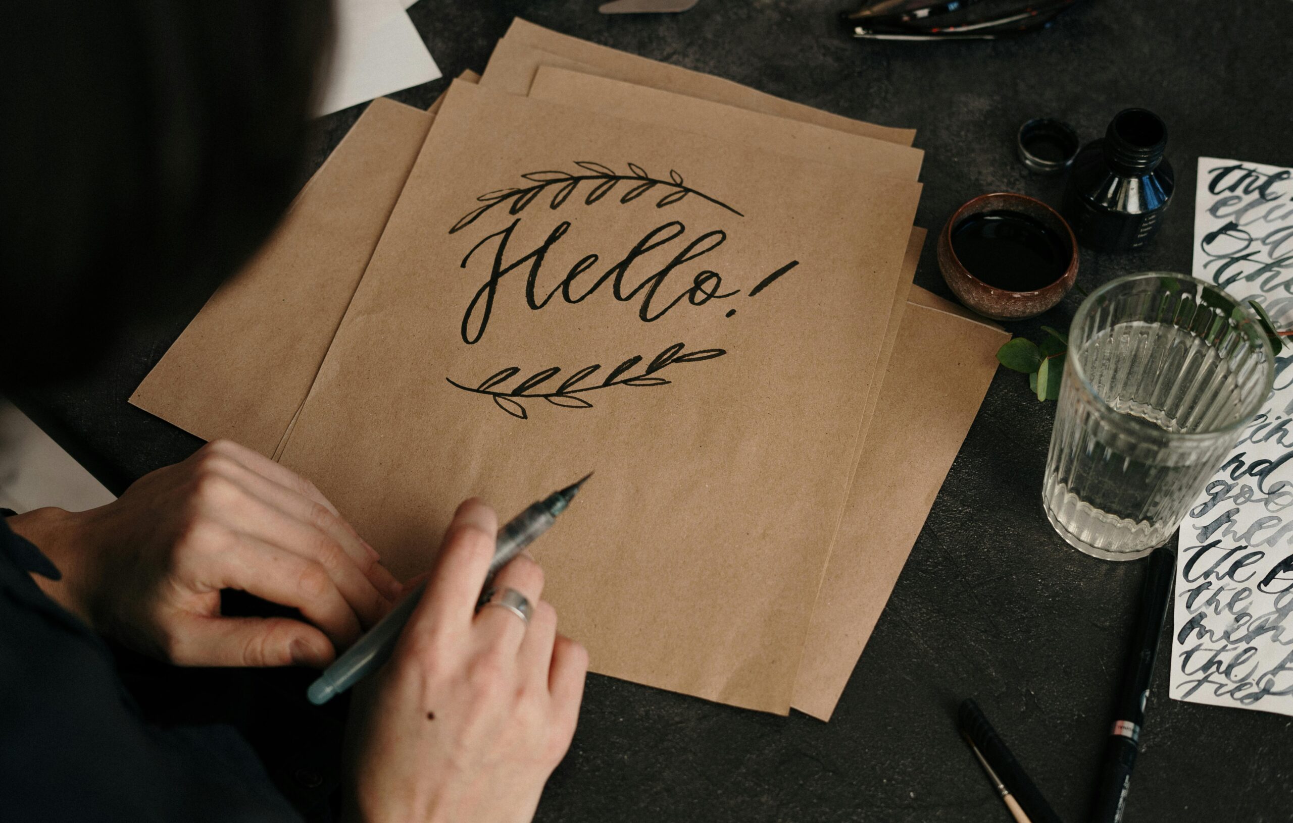 Artistic calligraphy of 'Hello!' on kraft paper with ink and pen. Perfect for stationery and craft themes.