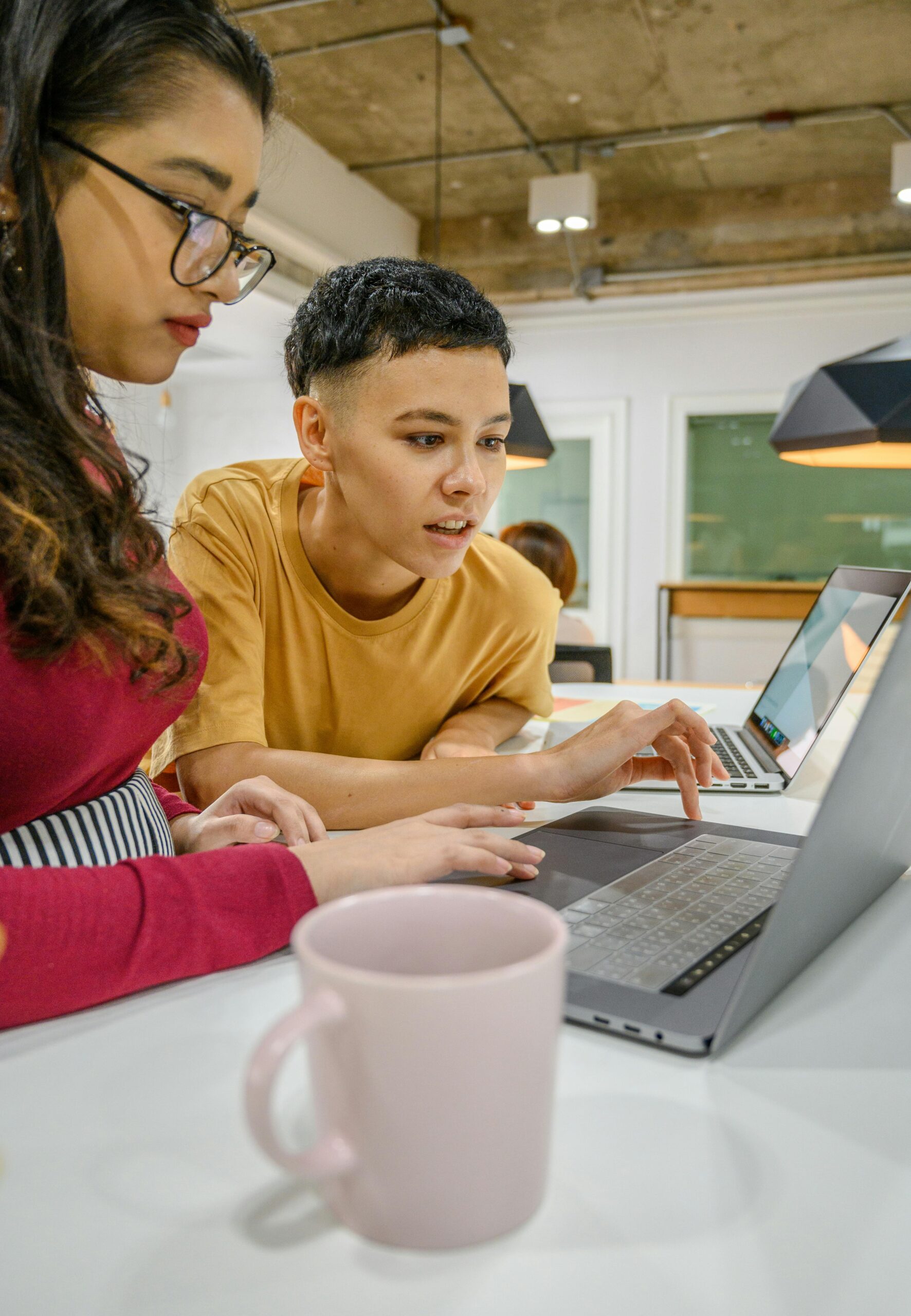 Two colleagues collaborating on a laptop in a modern office, demonstrating teamwork and focus.
