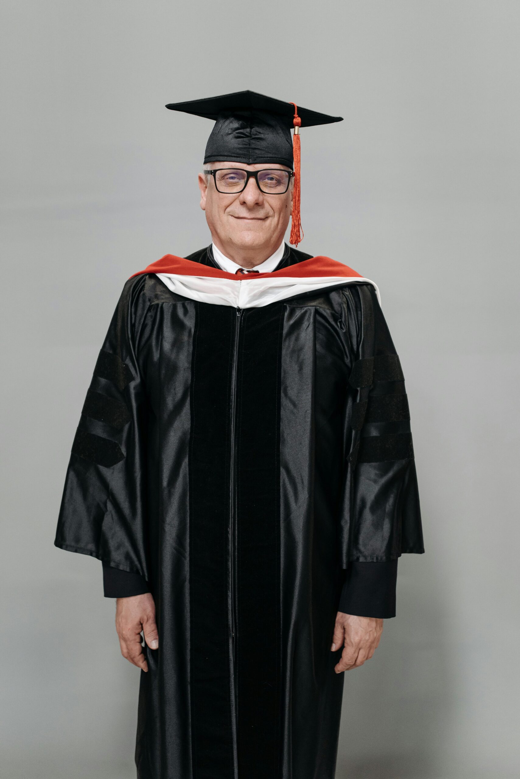 Smiling senior man wearing a graduation gown and cap, studio shoot.